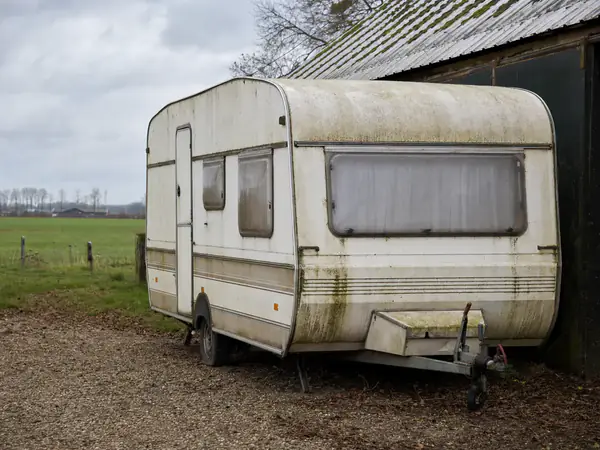 Oude verweerde caravan met een lekke band op het erf van een boerderij