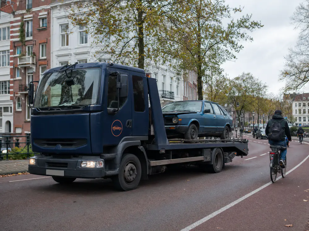 Autoambulance met een oude blauwe auto rijdt door een stadsstraat met fietspad